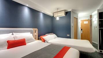 Habitación de hotel con dos camas, una almohada roja, una manta gris y una almohada blanca, además de una lámpara en el techo.