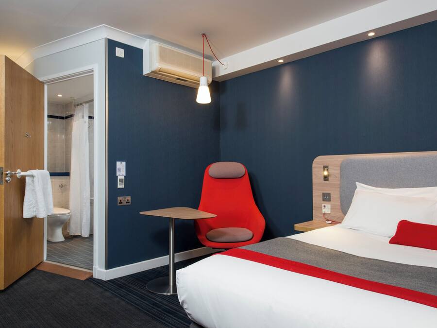 A hotel room with a bed, a red chair, a small table, and a shower area.
