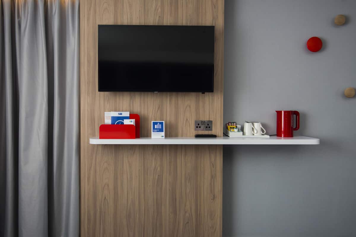 A modern room with a mounted TV, a white shelf with various items, and a grey curtain.