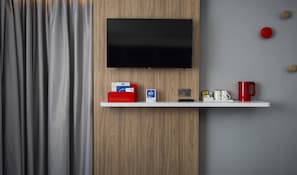 A modern room with a mounted TV, a white shelf with various items, and a grey curtain. - Holiday Inn Express London Luton Airport by IHG (Luton)