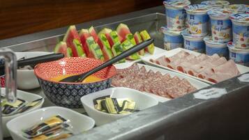 A buffet with sliced watermelon, various meats, and containers of yogurt.