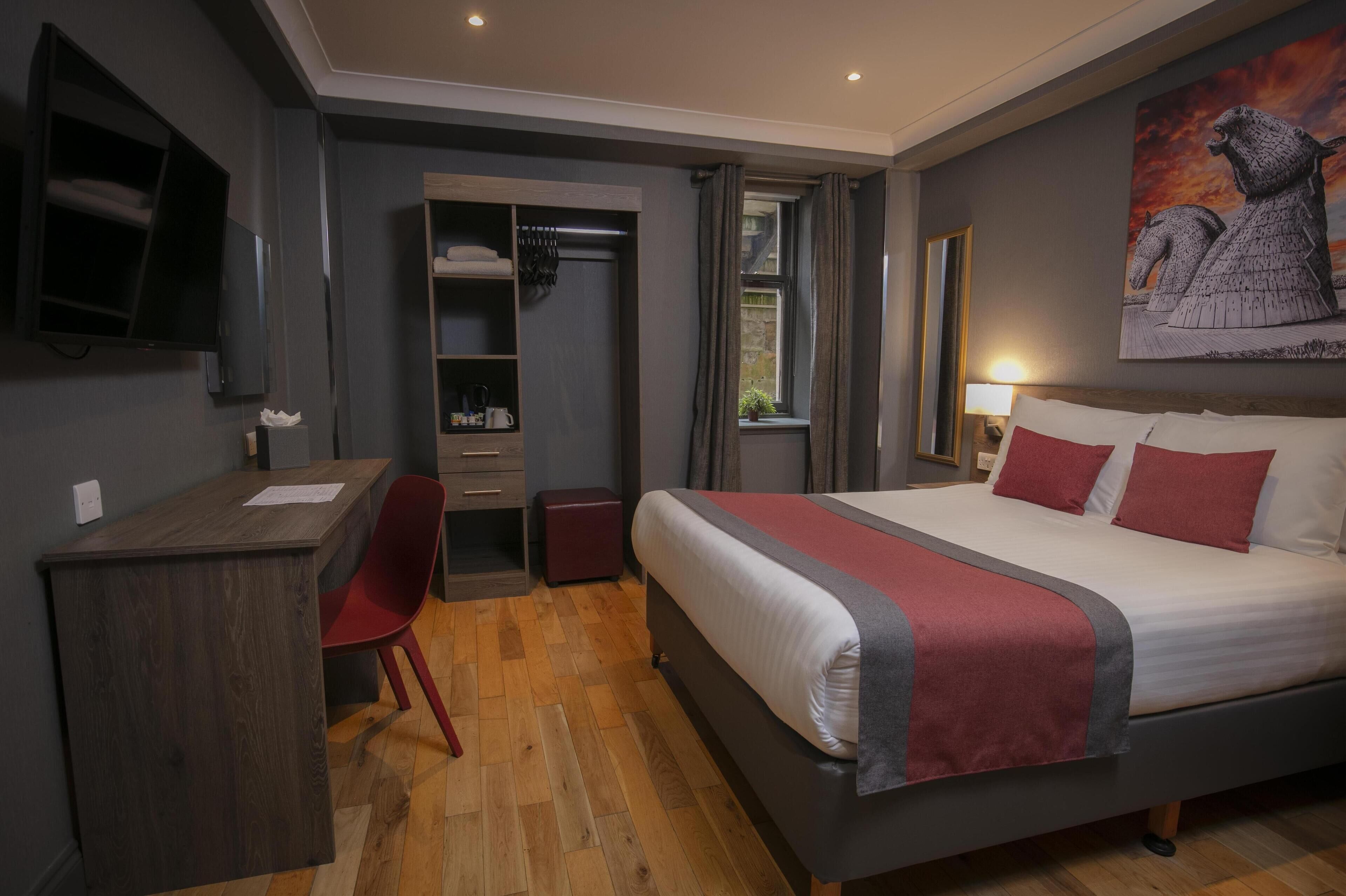 A bedroom with a bed, a desk, a chair, a wardrobe, and a painting on the wall.