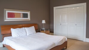 A neatly made bed with white linens, a wooden headboard, a bedside table with a lamp, a framed abstract painting, and a set of white double doors. - Dreamhouse Apartments Glasgow West End (Glasgow)