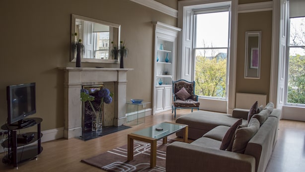 A living room with a fireplace, a television, a sofa, and a large window offering a view of trees. - Dreamhouse Apartments Glasgow West End (Glasgow)