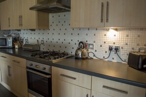 Une cuisine avec des meubles de rangement en bois, une cuisinière à gaz, un four à micro-ondes et un grille-pain.