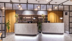 Un área de recepción con dos mostradores curvos, estanterías de madera y plantas en macetas.