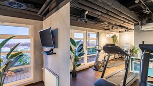 Un gimnasio moderno con cinta de correr, bicicleta estática y amplios ventanales con vista a la ciudad.