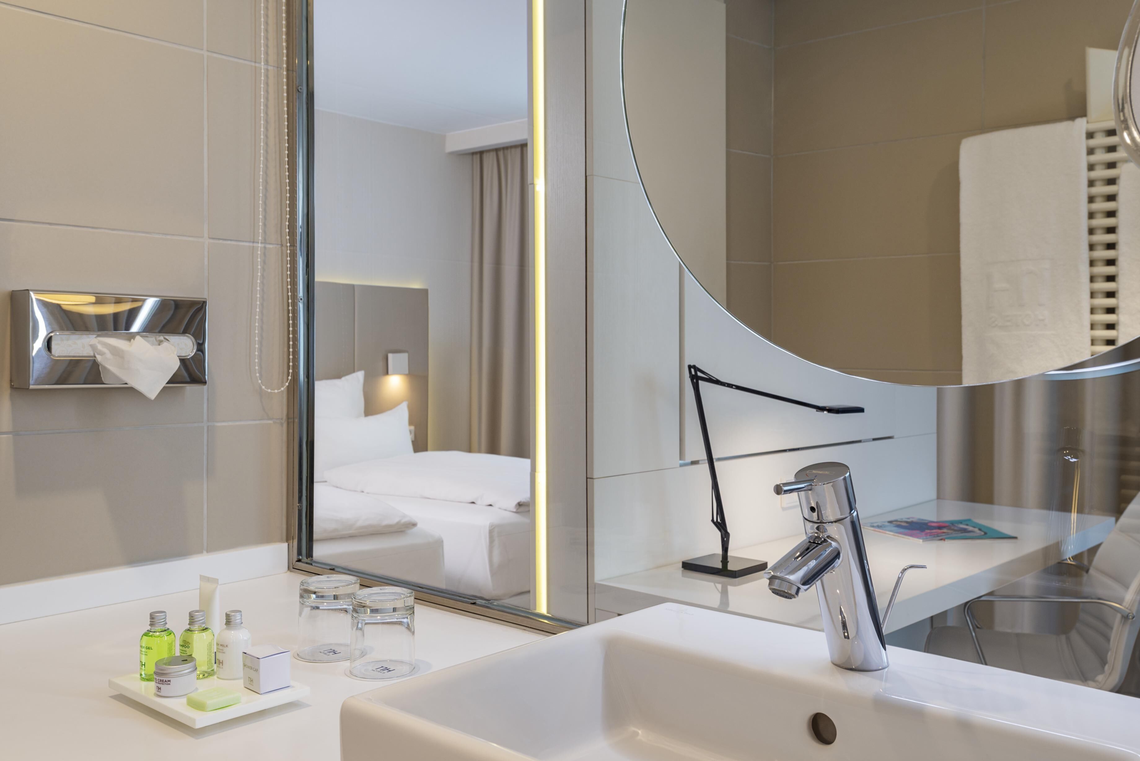 A modern hotel bathroom with a large mirror, a sink, and toiletries.
