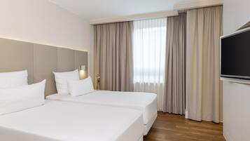 Quarto de hotel com duas camas, uma televisão e uma janela com cortinas.