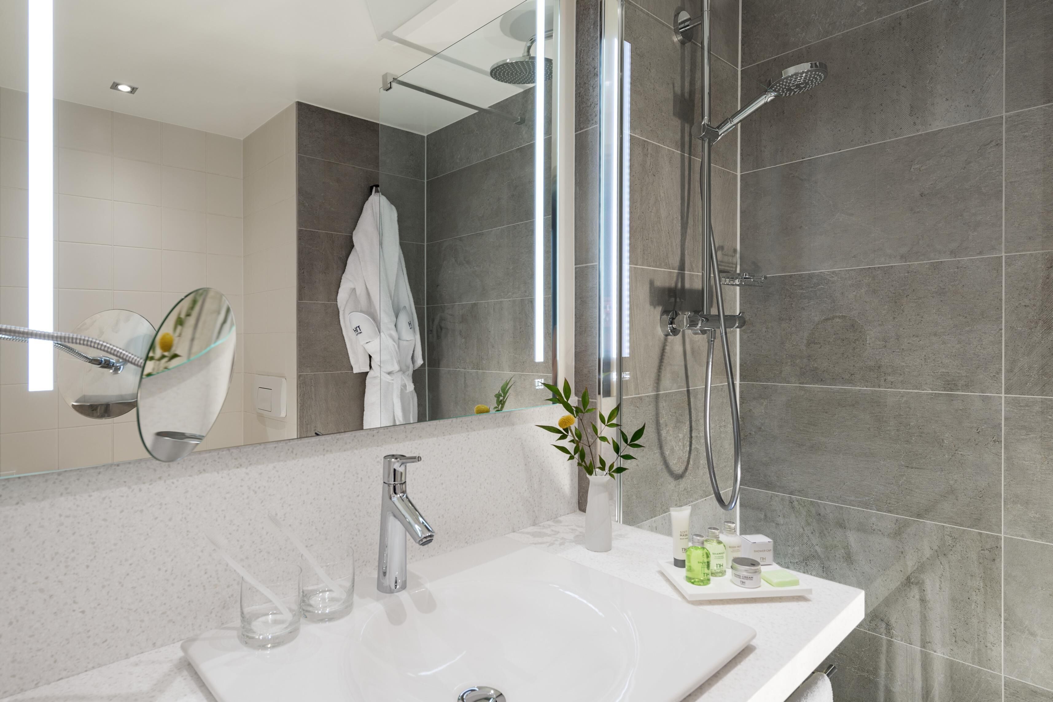 A modern bathroom with a large mirror, a white sink, a shower with a handheld showerhead, and a glass shower enclosure.