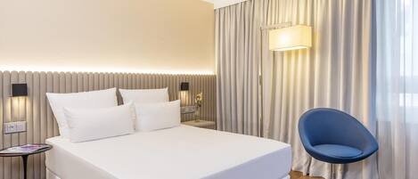 Una habitación de hotel con cama, mesita de noche, lámpara, silla y cortinas.