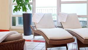 Una habitación con dos sillones de mimbre con cojines blancos, una planta grande en maceta y vistas a través de una ventana.
