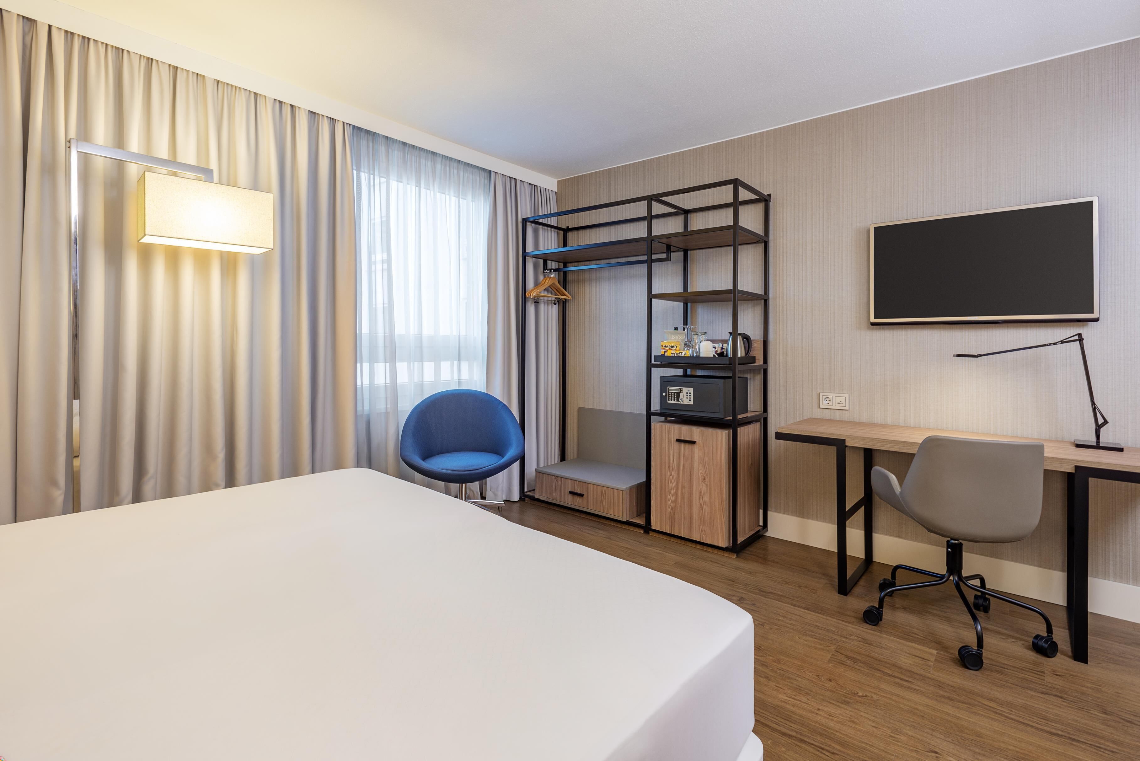 A hotel room with a bed, a desk, a chair, a wardrobe, and a TV.
