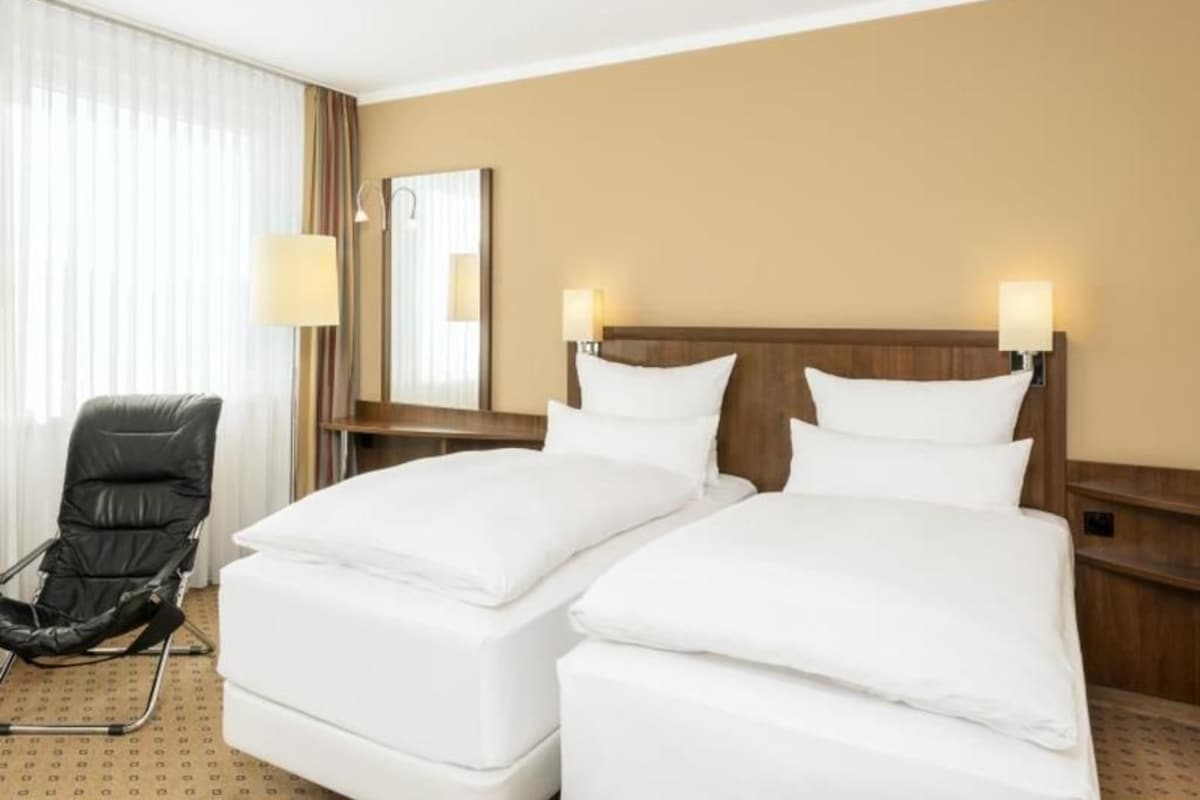 A hotel room with two beds, a chair, a lamp, and a mirror.