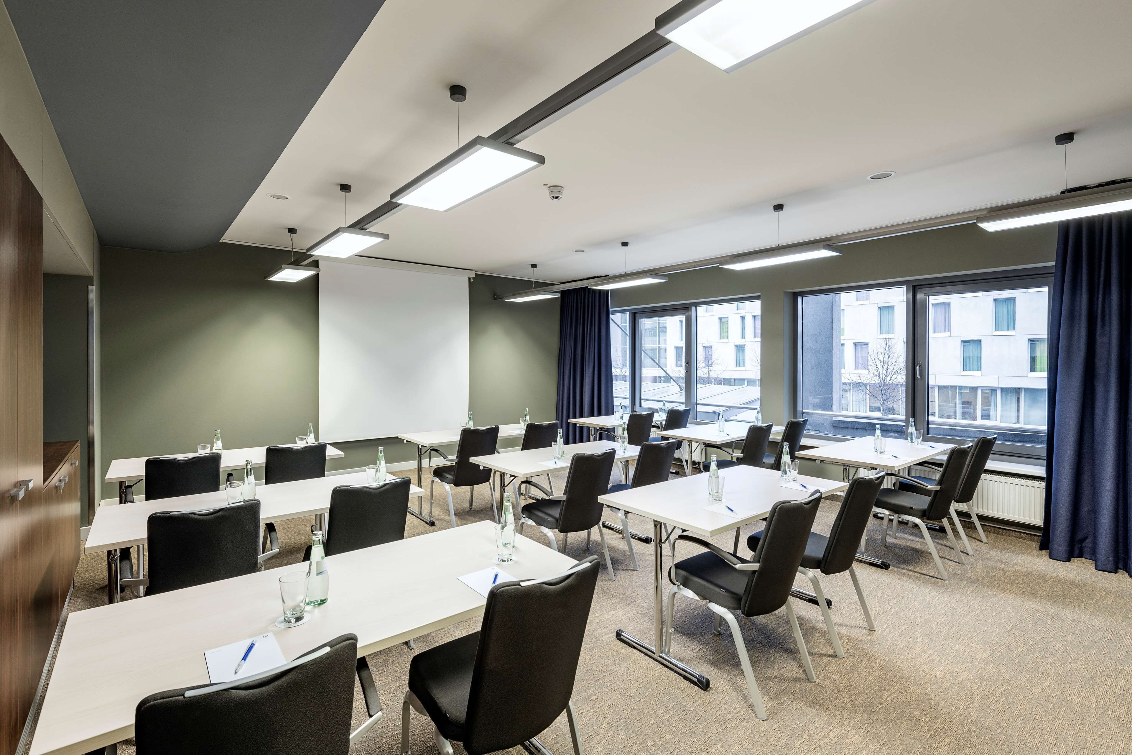 Una sala de conferencias con varias mesas y sillas, ventanas amplias con cortinas y una pizarra.
