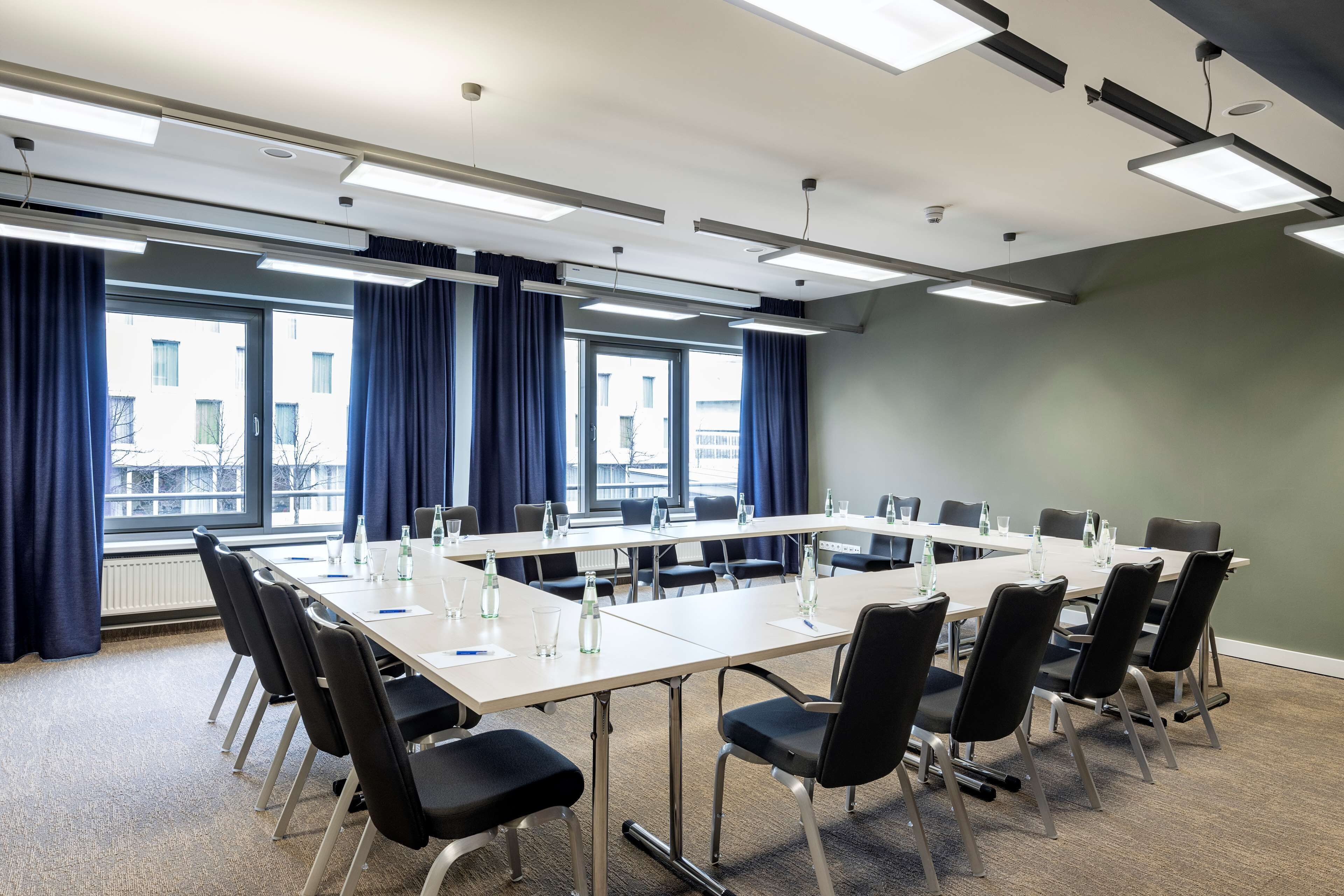 Une salle de conférence avec une longue table, des chaises noires et une vue sur les bâtiments à travers de grandes fenêtres.