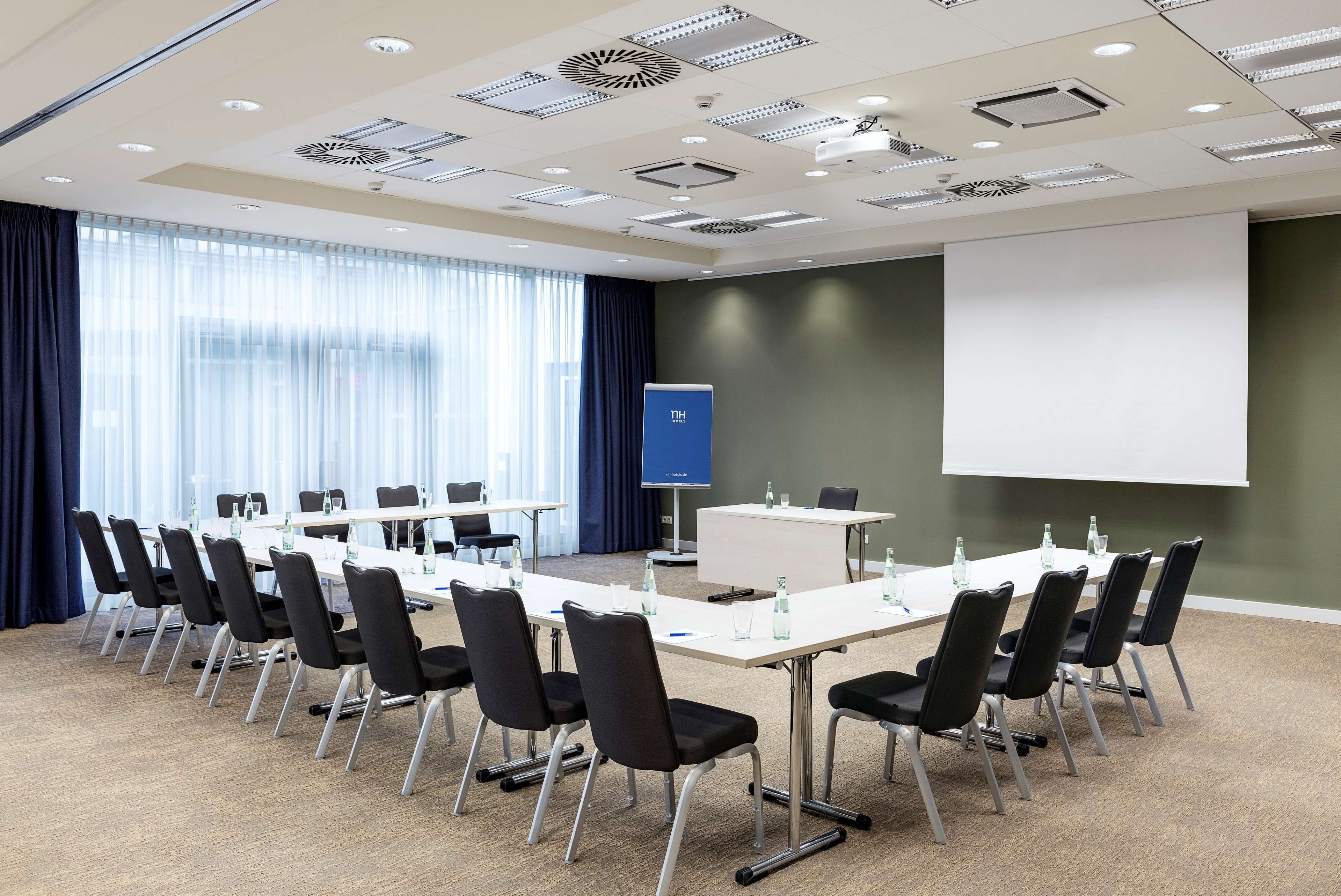 A conference room with a long table, chairs, a projector screen, and a presentation screen.