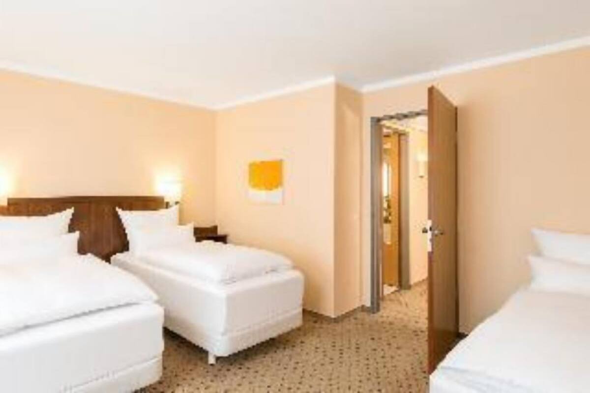 A hotel room with two beds, a wooden headboard, a wall-mounted light, and a door leading to another room.