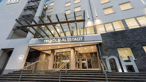 En modern hotellentrén med en trappa som leder upp till dörrarna, en tydlig skylt med texten ”NH KÖLN ALSTADT” och en glasfasad.