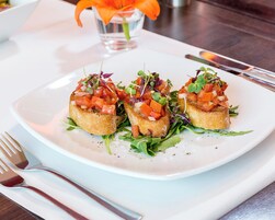 Ein Teller mit Essen, darunter ein weißer Teller, drei Brotscheiben mit Gemüse und ein kleines Glas Wasser mit einer orangefarbenen Blüte.