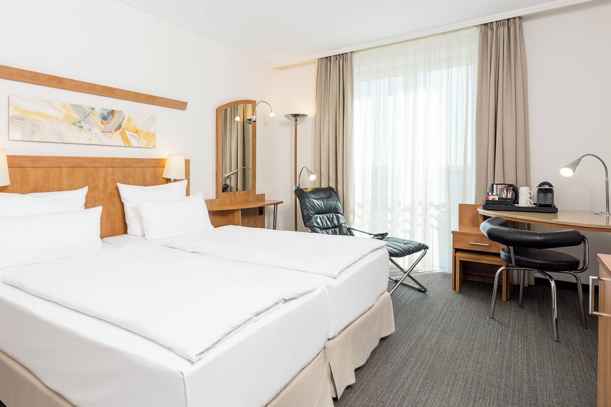 A hotel room with a large bed, a desk, a chair, a lamp, and a mirror.