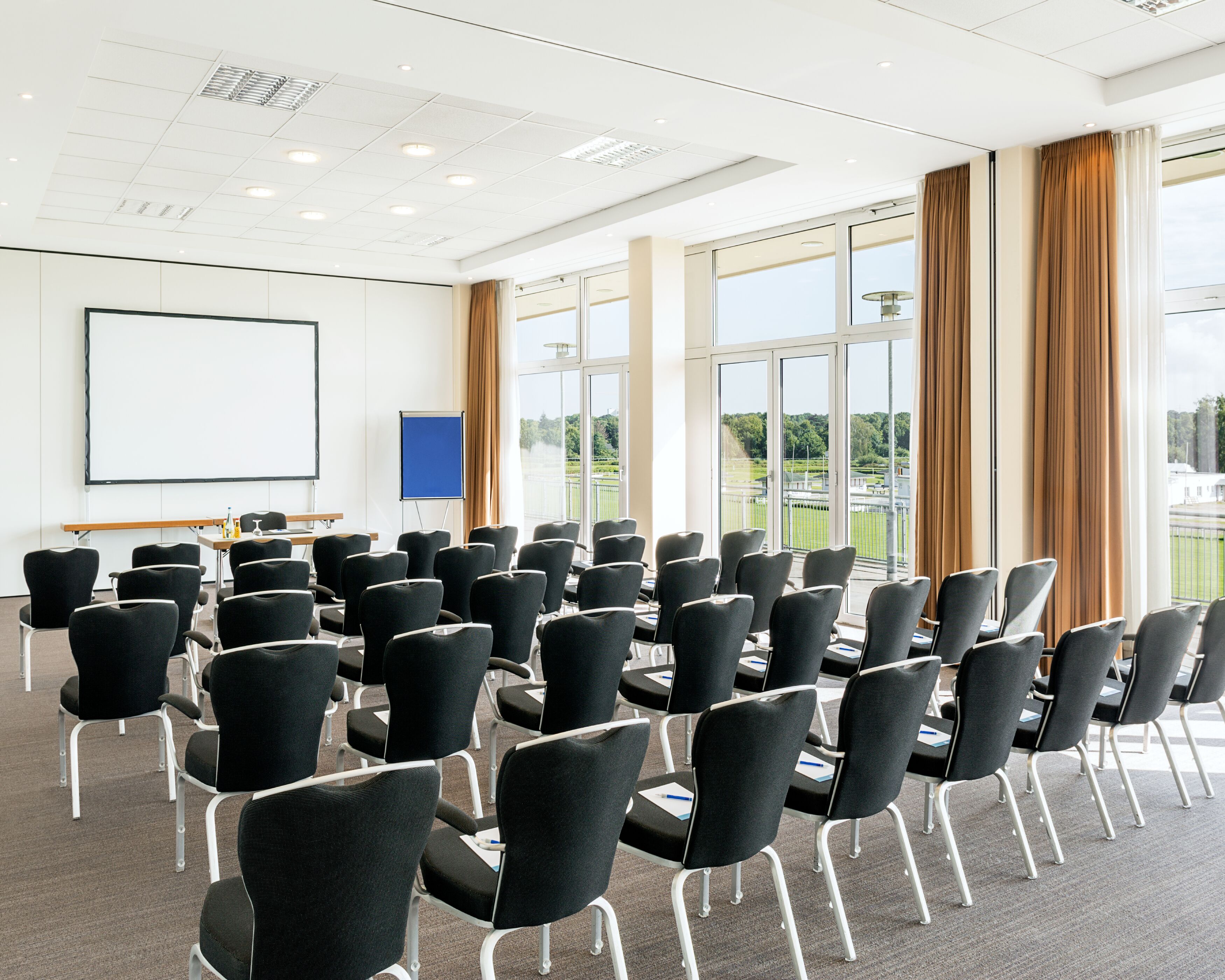 Un salón de conferencias con filas de sillas, una pizarra y ventanas amplias con cortinas.