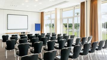 Un salón de conferencias con filas de sillas, una pizarra y ventanas amplias con cortinas.