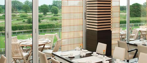 Un comedor con mesas dispuestas para cuatro, ventanas amplias y vistas a un paisaje verde.