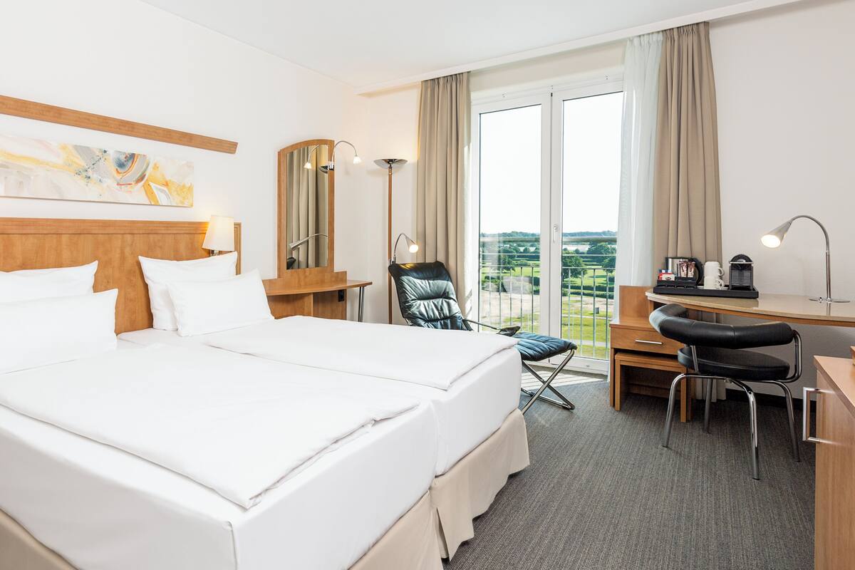 A hotel room with a large bed, a desk with a chair, a mirror, and a view of the outdoors.