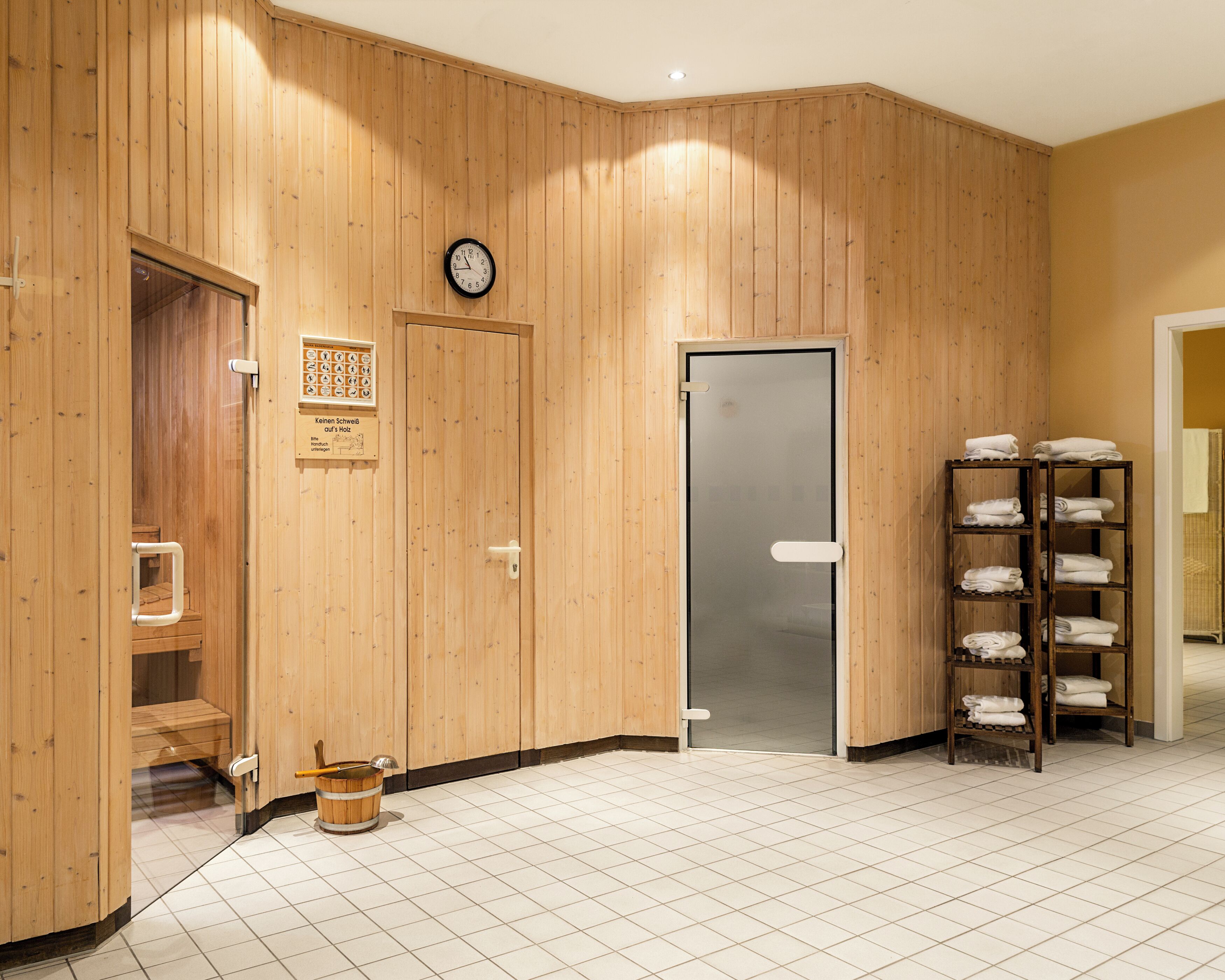 A wooden interior with a sauna, a clock, and a towel rack.