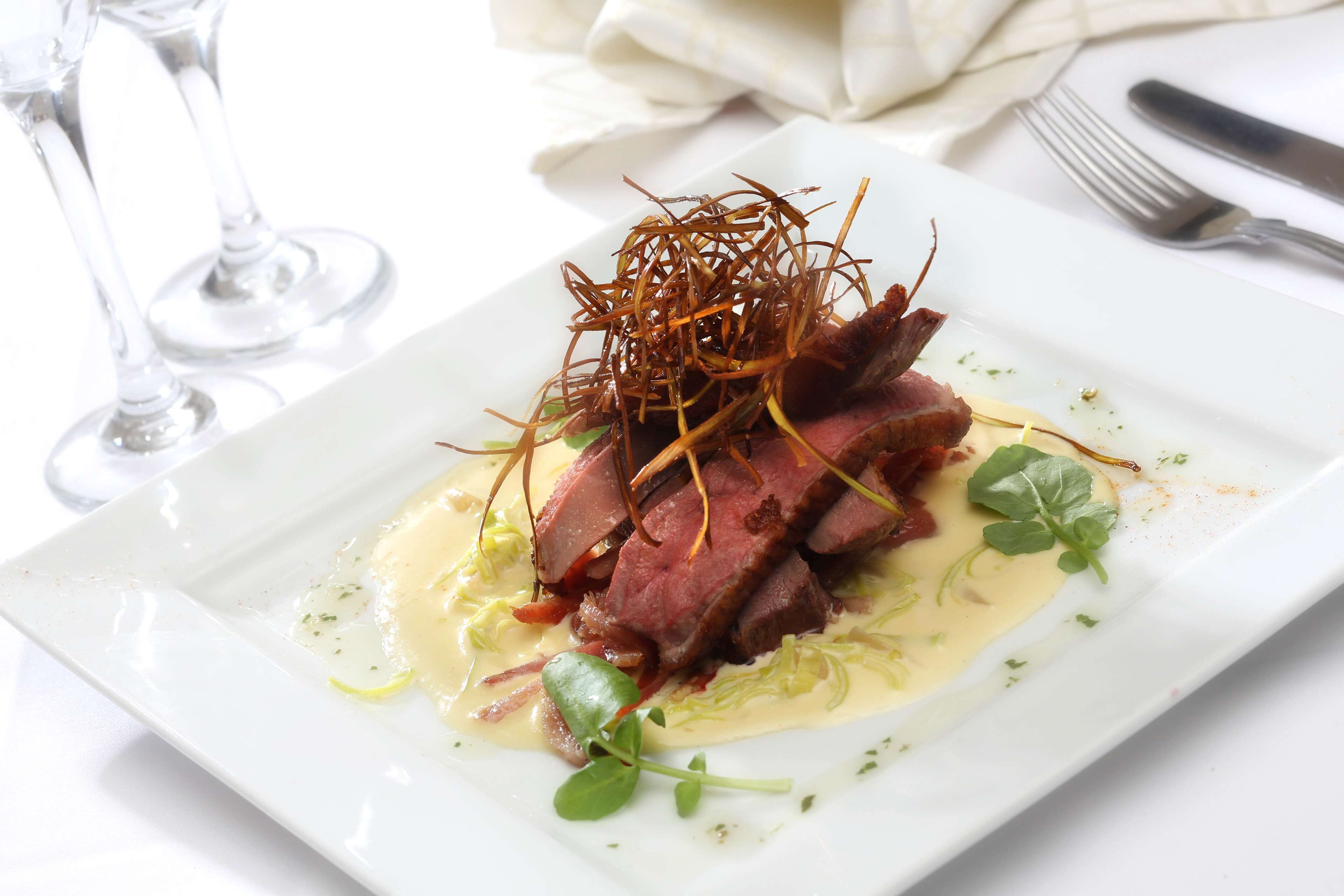 En hvid tallerken med en portion skiveskåret kød, grønt og en cremet sauce.