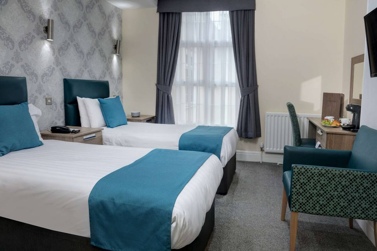 Ein Hotelzimmer mit zwei Betten, einem Schreibtisch, einem Stuhl und einem Fenster mit Vorhängen.