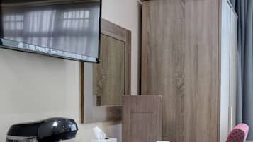 A hotel room with a wooden desk, a coffee maker, a plate of fruit, a red chair, and a television on the wall.