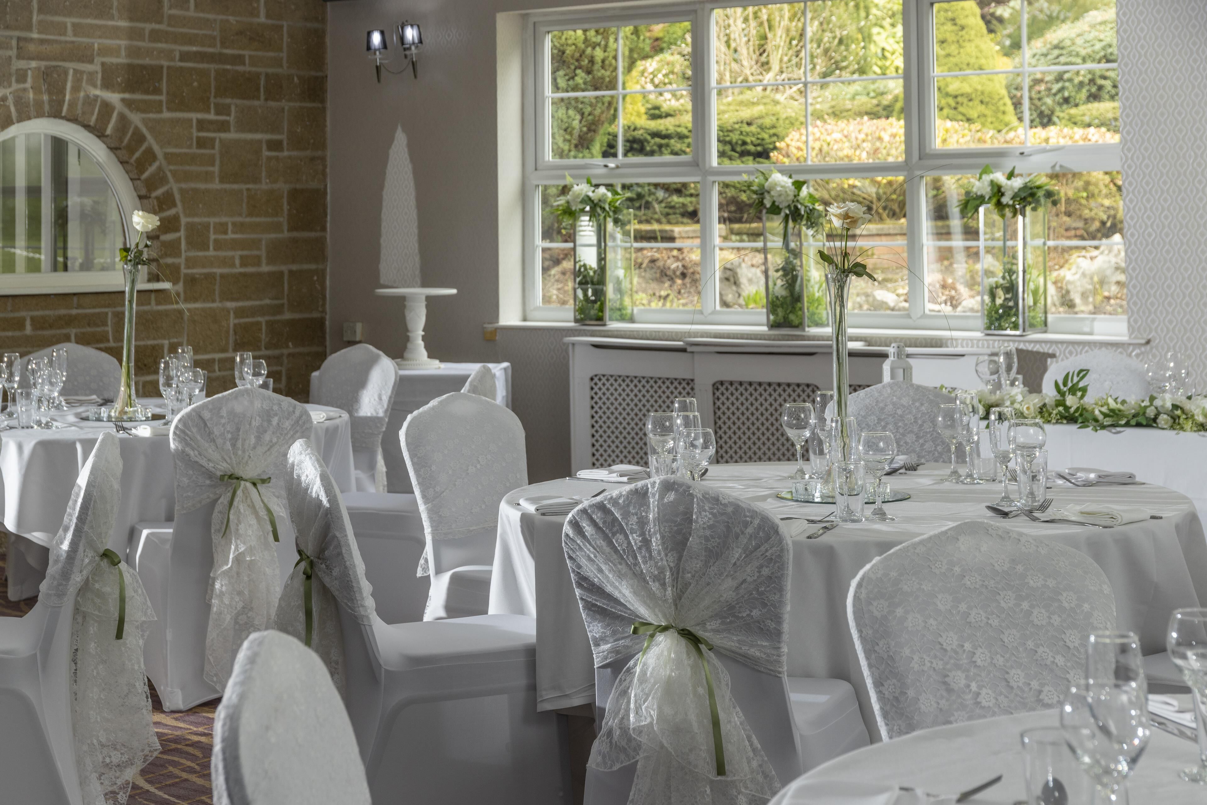 A dining area with white tables and chairs, a brick wall, and a window with a view of greenery.