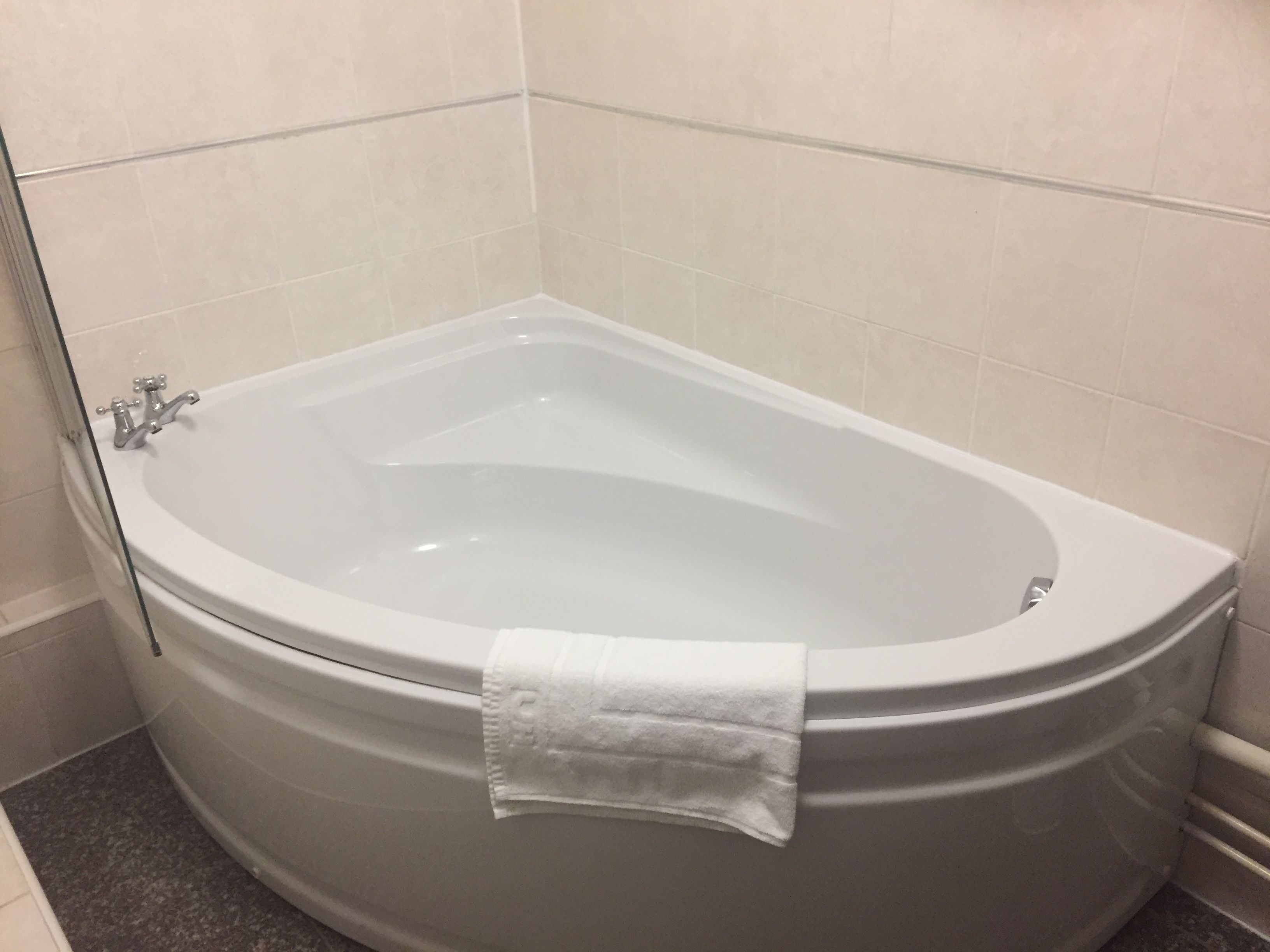 Un baño moderno con una bañera independiente, una toalla colgada al costado y paredes de azulejos.