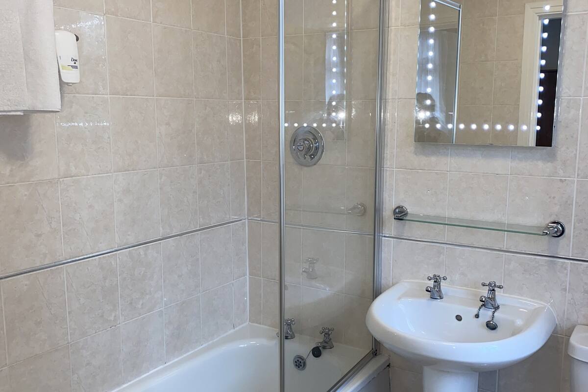 Ein modernes Badezimmer mit einer in Glas eingefassten Dusche, einem weißen Waschbecken und einem großen, beleuchteten Spiegel.