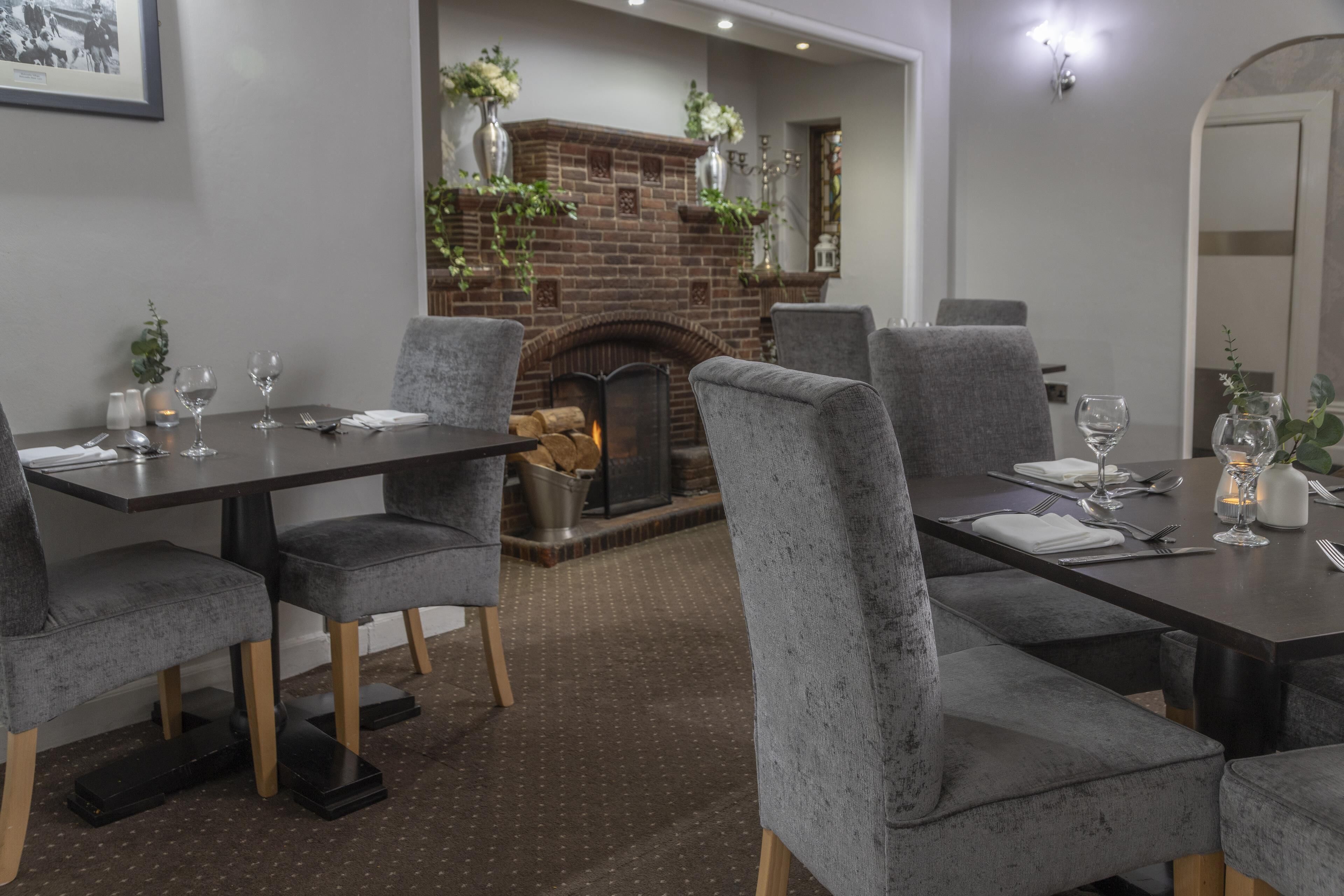 A dining area with a brick fireplace, grey upholstered chairs, and a polished wooden floor.