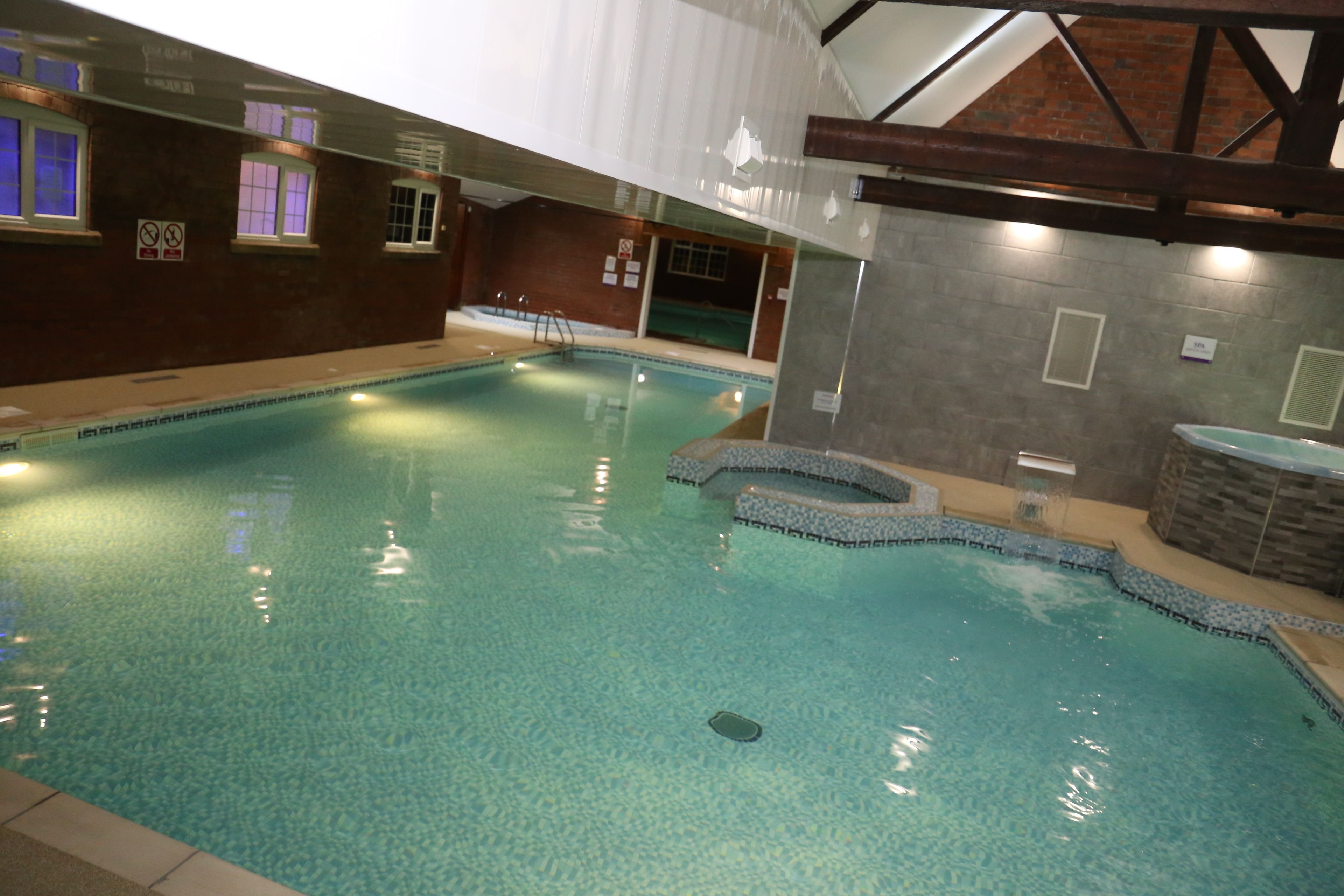 Una piscina interior con agua cristalina, escalones de acceso y una pared de ladrillo con ventanas.