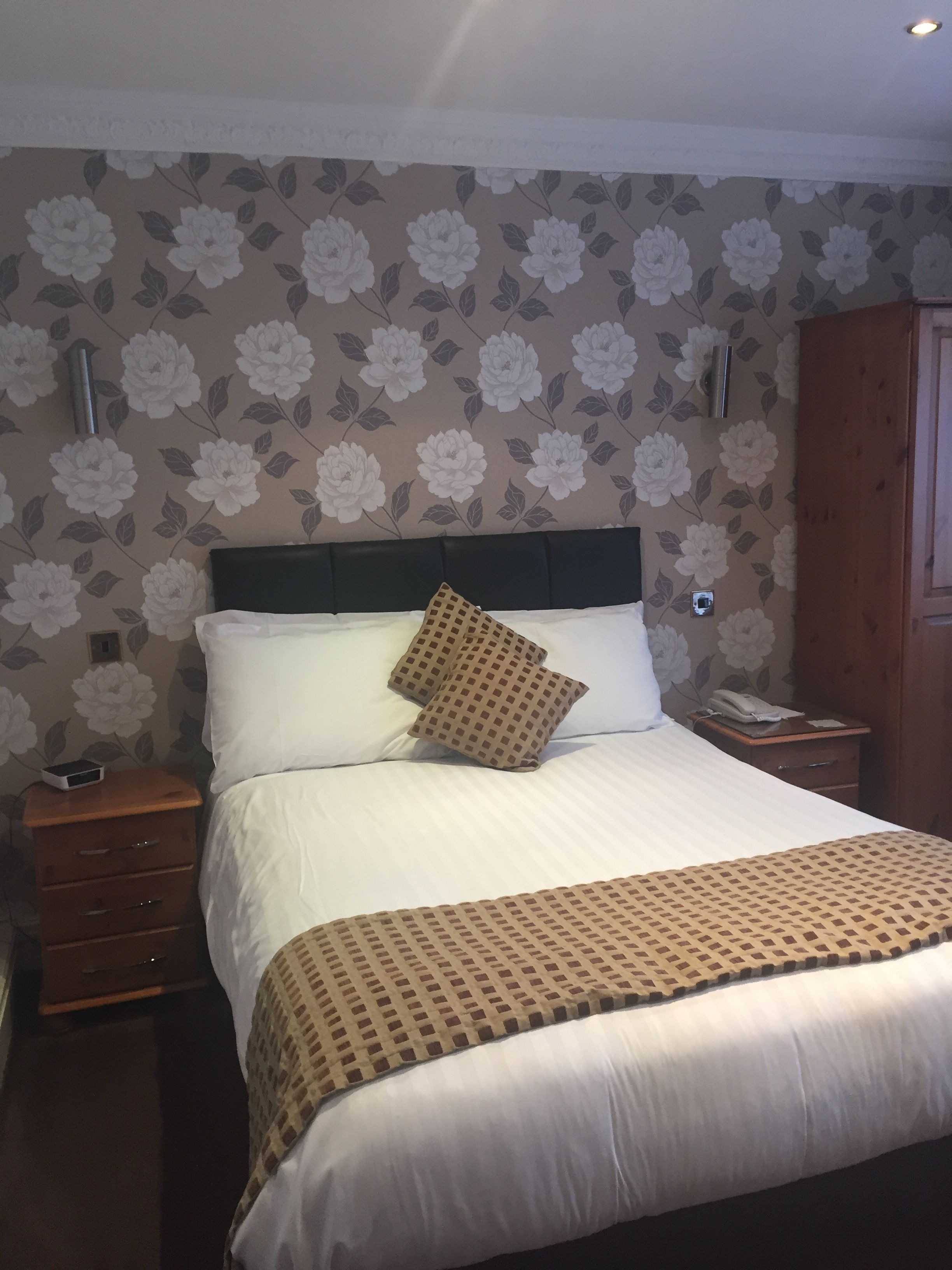A neatly made bed with a patterned bedspread, a pillow, and a bedside table with a phone and a small device.