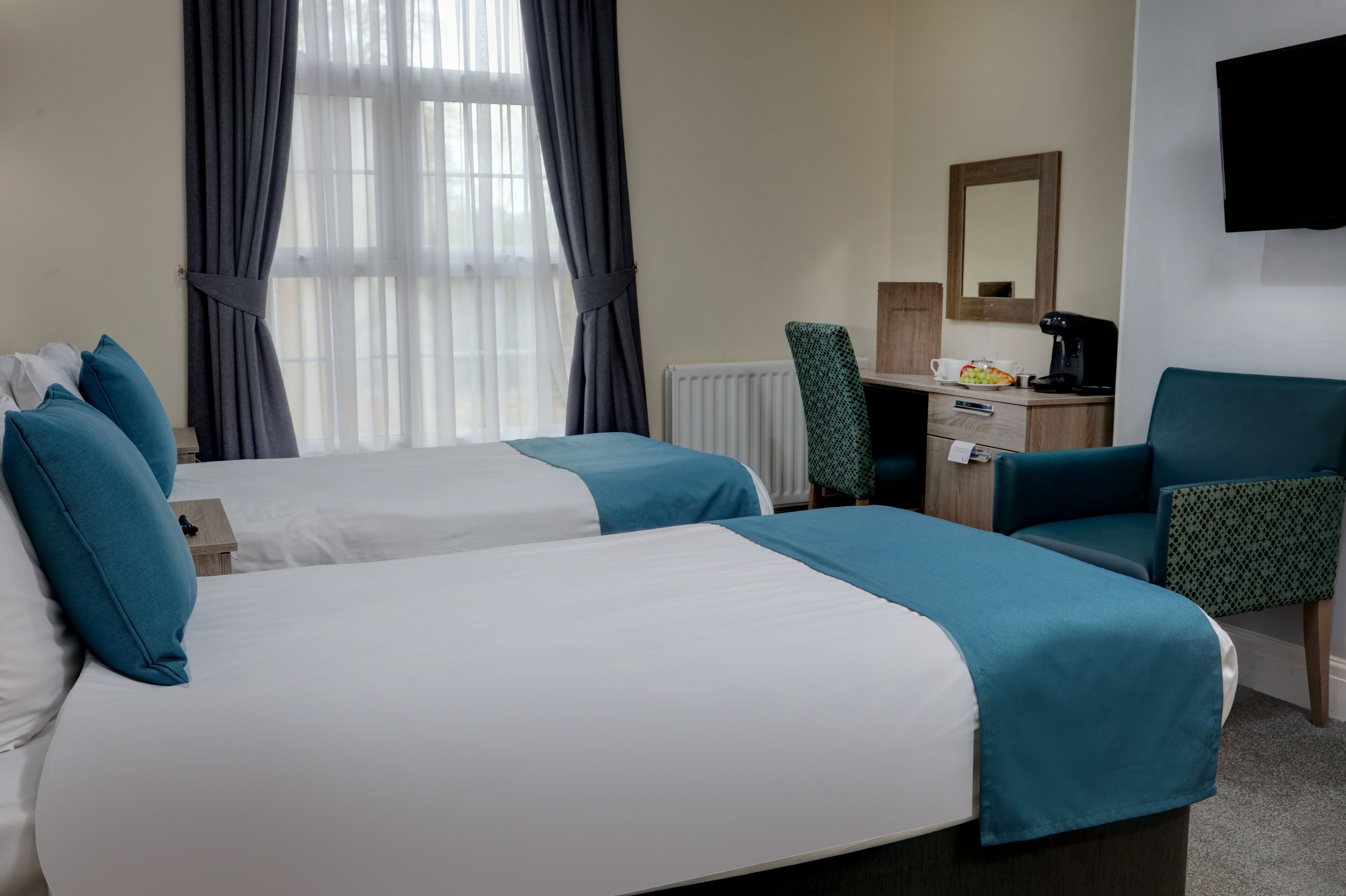 A hotel room with two beds, a desk with a chair, a coffee maker, and a TV on the wall.