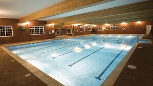 Una piscina cubierta con múltiples carriles, vigas de madera en el techo e iluminación empotrada en las paredes.