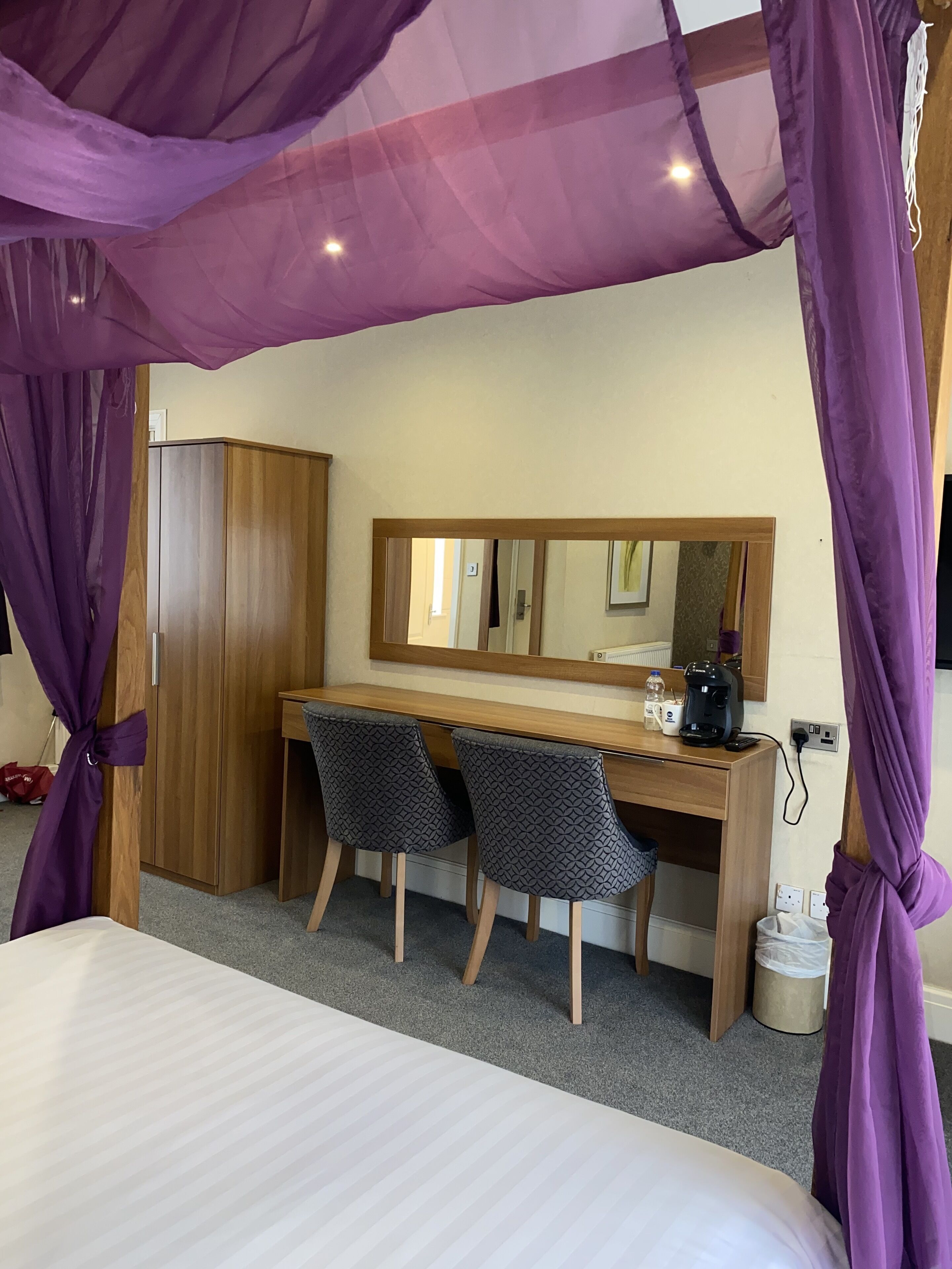A bedroom with a bed, a desk with two chairs, a wardrobe, and a large mirror.