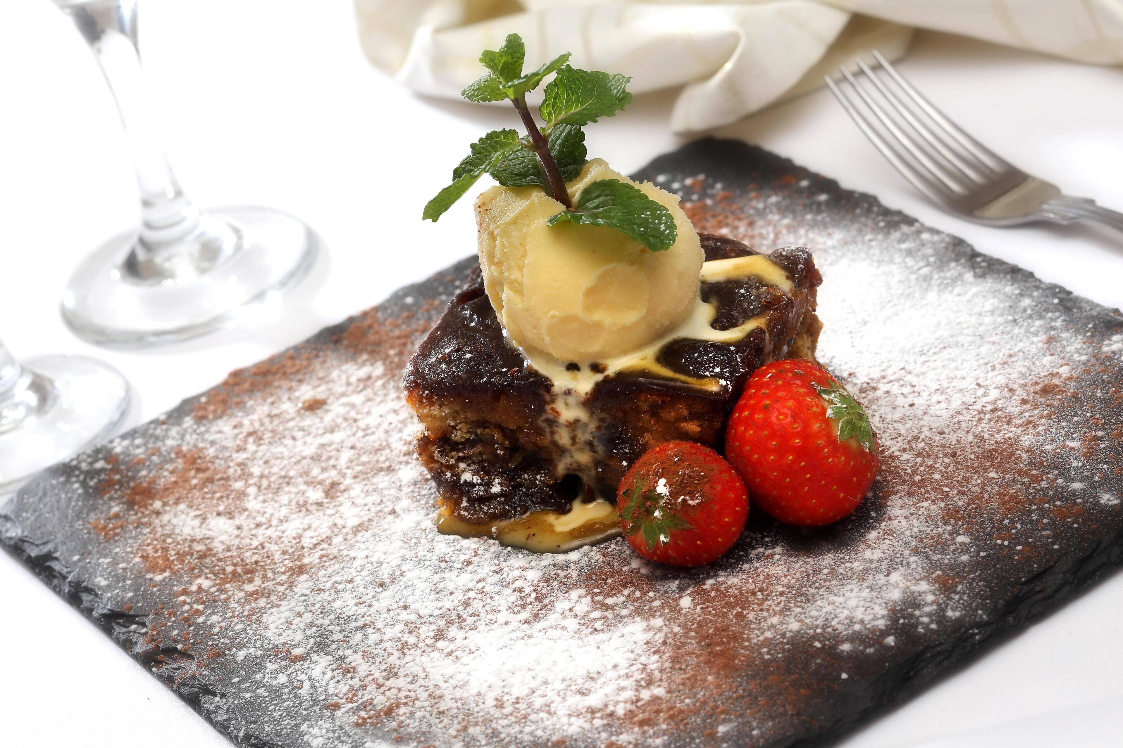 Un dessert composé de glace, de fraises et de menthe, servi sur une assiette en ardoise.