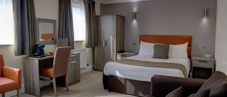 A hotel room with a bed, a desk, a chair, a wardrobe, and a sofa.