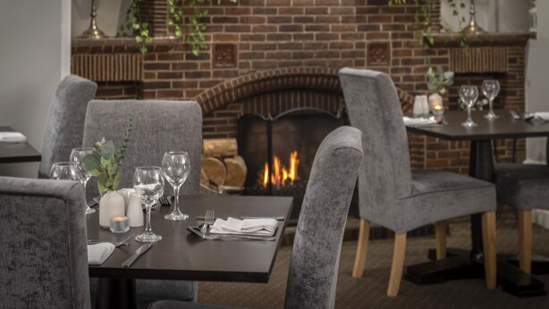 Un restaurante con sillas tapizadas en gris, una chimenea de ladrillo y una mesa dispuesta para comer.