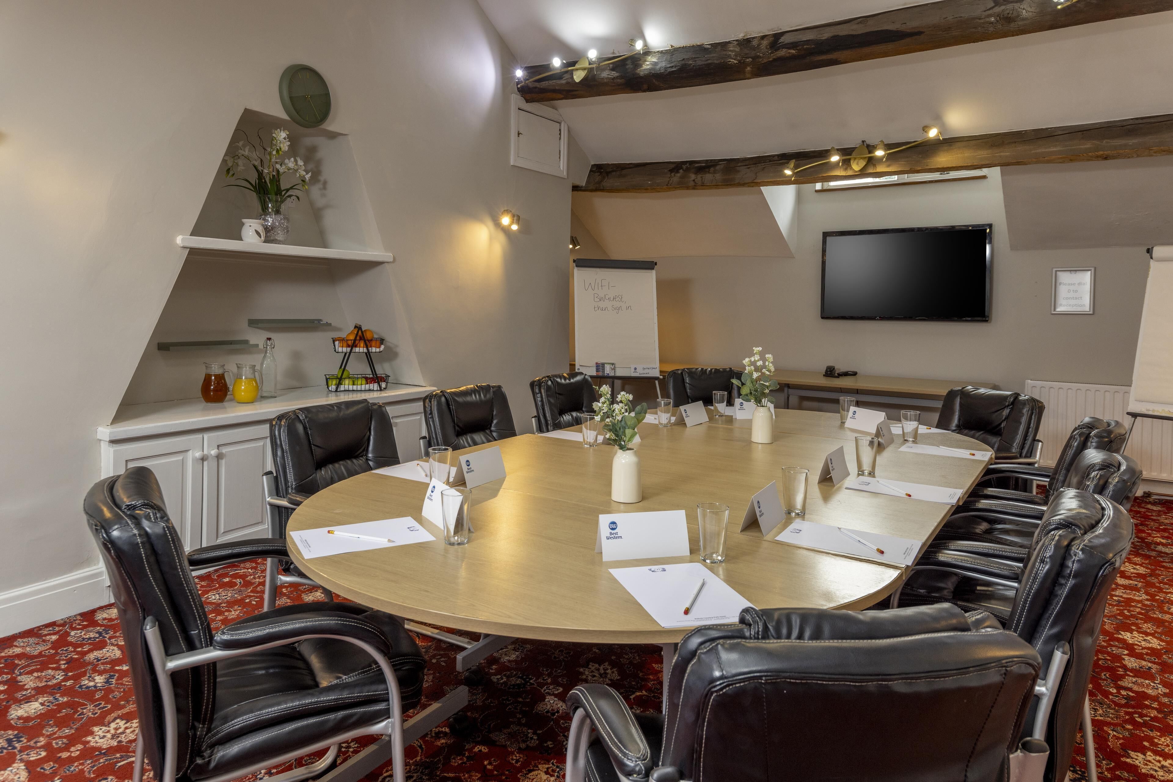 A conference room with a round table, black leather chairs, nameplates, a whiteboard, and a flat-screen TV.