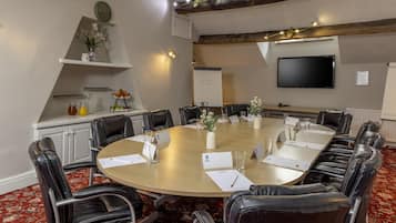 A conference room with a round table, black leather chairs, nameplates, a whiteboard, and a flat-screen TV.