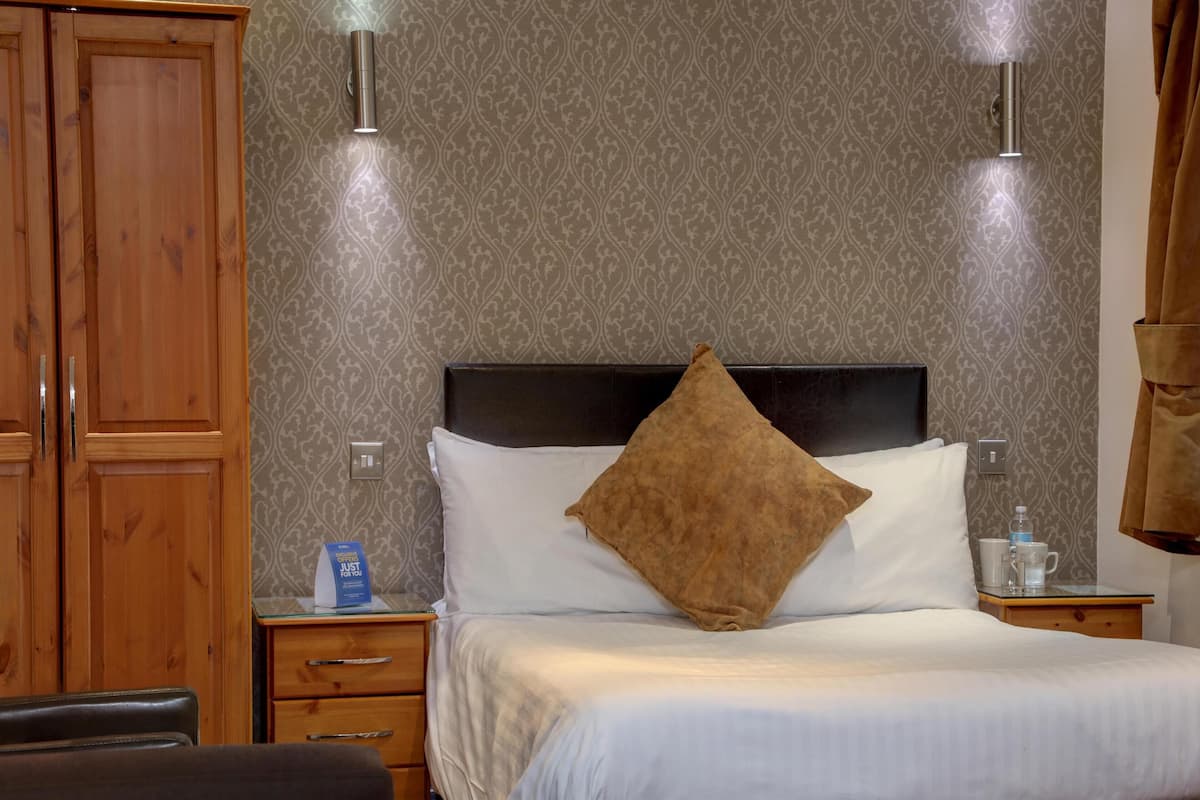 Ein Hotelzimmer mit einem Bett, einem Holzschrank und einem Nachttisch mit Wasserflasche und Glas.