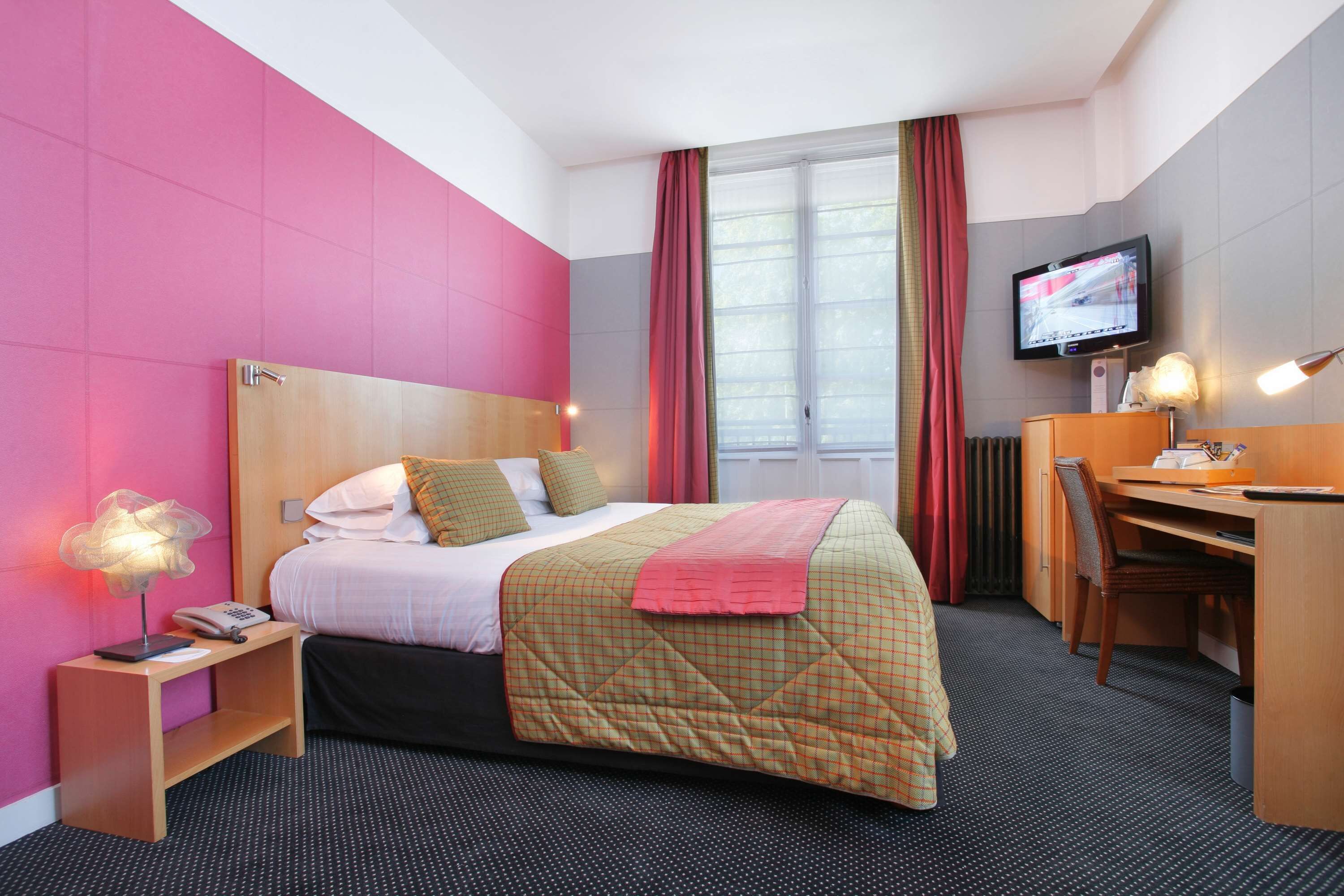 A hotel room with a bed, a desk, a television, and a window with curtains.