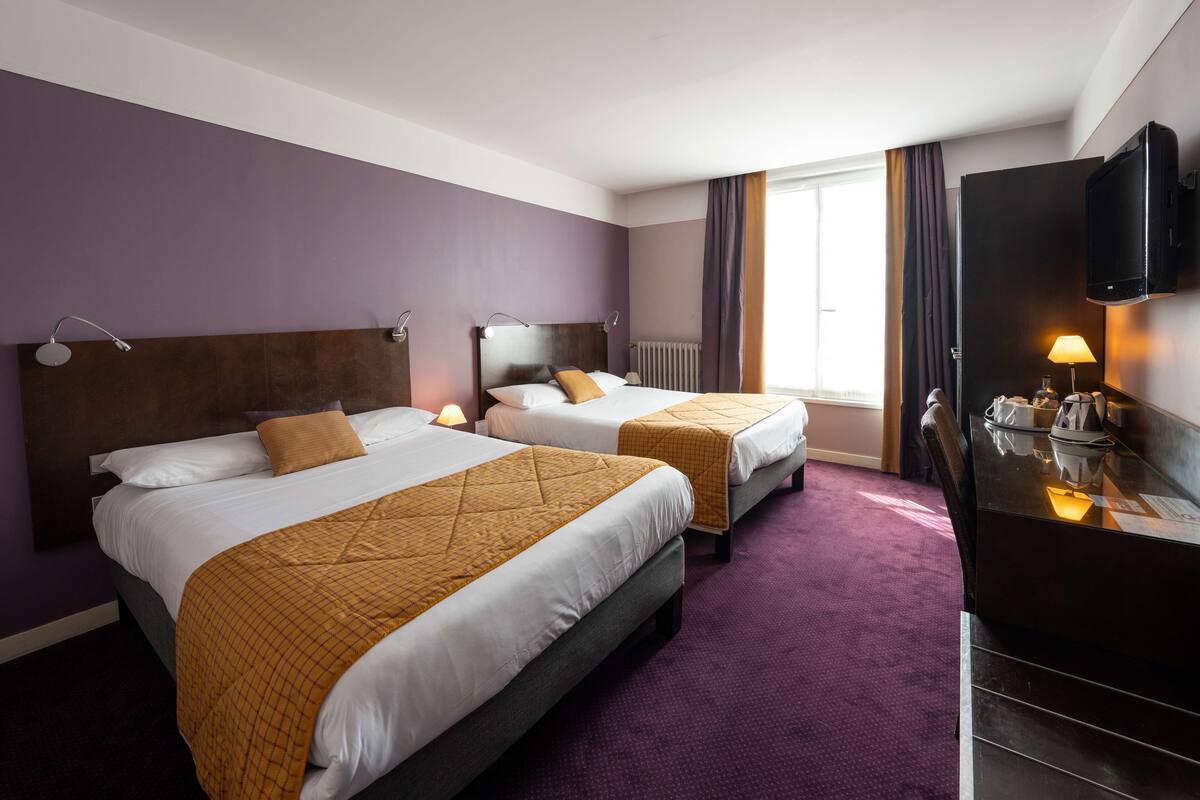 A hotel room with two beds, a TV, and a desk with a lamp.